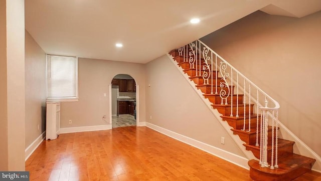 staircase with recessed lighting, baseboards, arched walkways, and wood finished floors