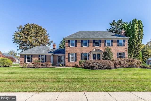 colonial-style house featuring a front yard, brick siding, and a chimney