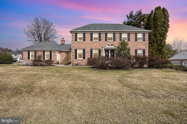 colonial-style house featuring brick siding, a lawn, and a chimney