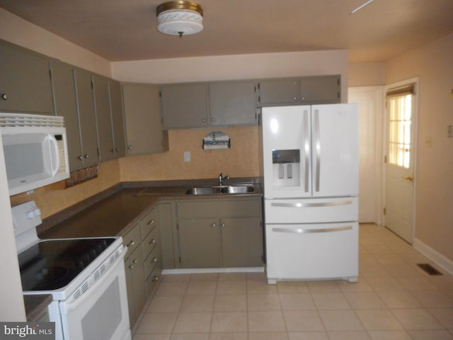 kitchen featuring dark countertops, white appliances, gray cabinetry, and a sink