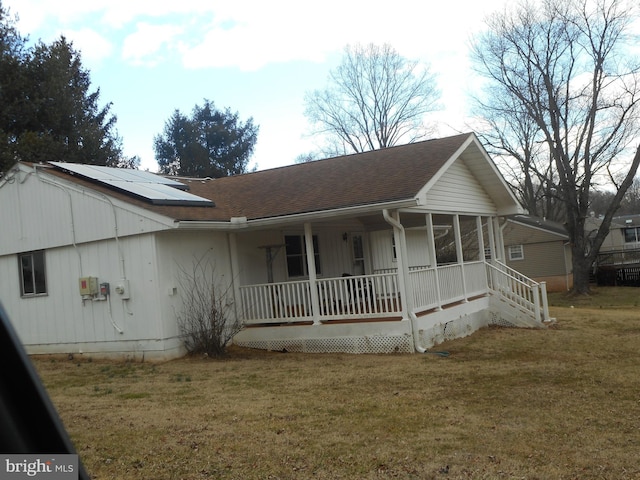 view of front of home with a sunroom, covered porch, a front yard, a shingled roof, and solar panels