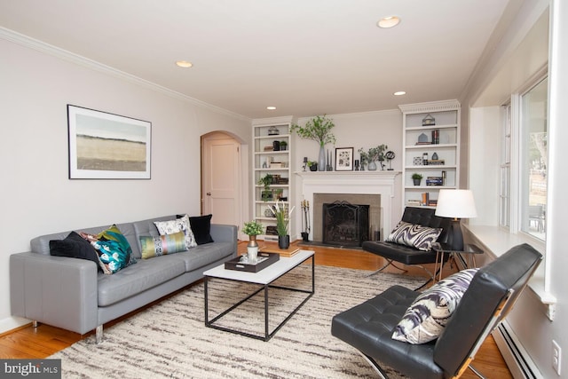 living area with arched walkways, wood finished floors, crown molding, and a baseboard radiator