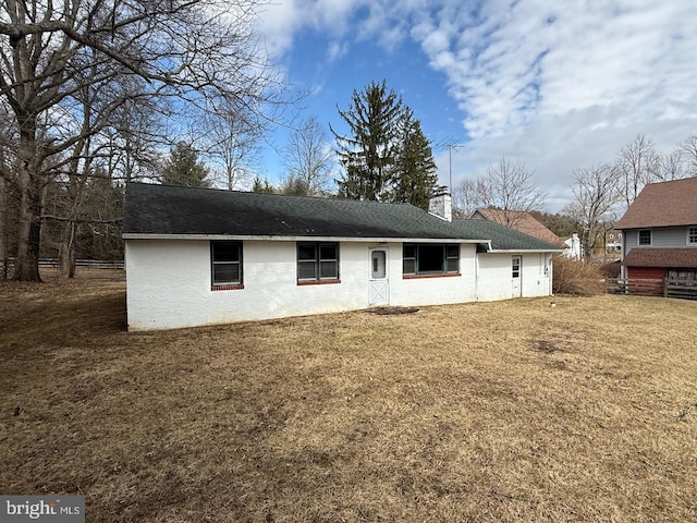 rear view of property featuring a yard, roof with shingles, a chimney, and stucco siding