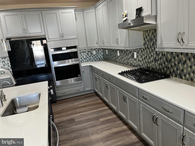 kitchen featuring dark wood-type flooring, under cabinet range hood, gray cabinets, appliances with stainless steel finishes, and a sink