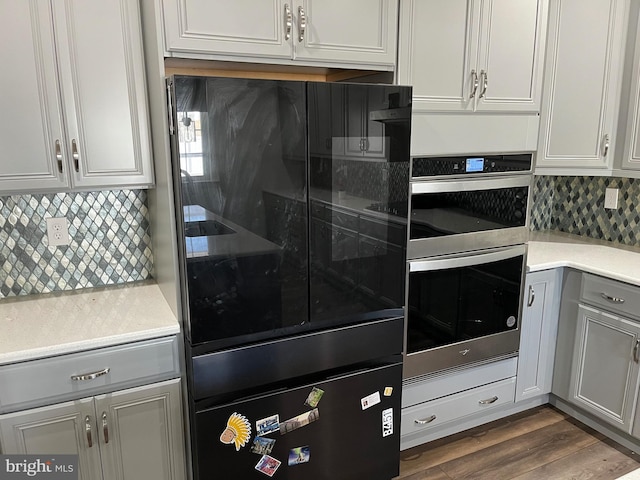 kitchen with stainless steel double oven, dark wood-type flooring, tasteful backsplash, and light countertops