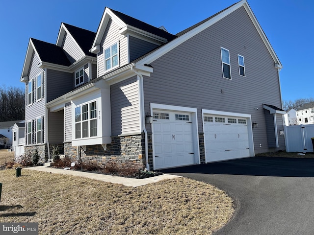 view of property exterior featuring an attached garage, stone siding, and driveway