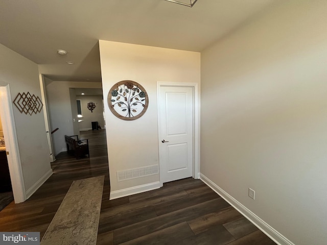 corridor featuring visible vents, baseboards, and dark wood-type flooring