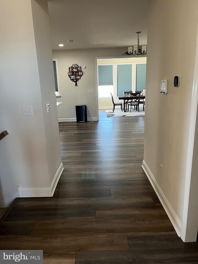 hallway featuring dark wood-style floors, a chandelier, and baseboards