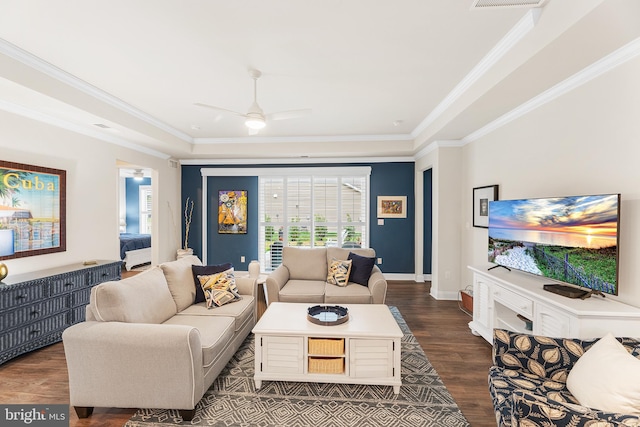 living room with dark wood-type flooring, a raised ceiling, ornamental molding, baseboards, and ceiling fan