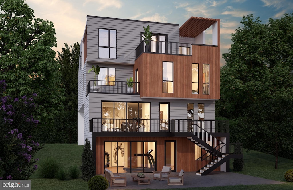 back of house at dusk featuring stairway, a balcony, a yard, and a patio area