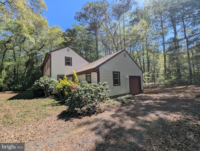 view of side of property featuring a garage, driveway, and roof with shingles