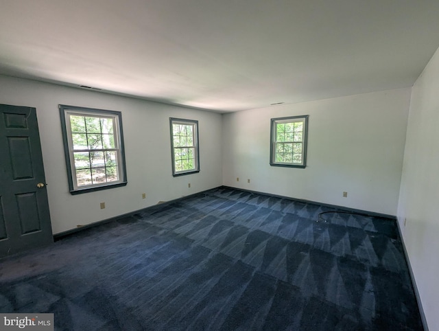 spare room featuring dark carpet and baseboards