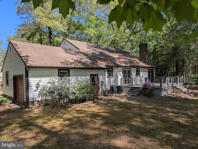 rear view of property with a garage, a deck, a chimney, central AC unit, and a shingled roof