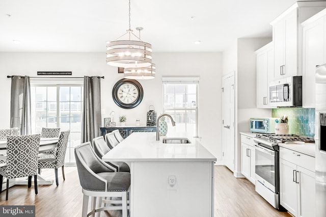 kitchen featuring light wood-type flooring, a sink, appliances with stainless steel finishes, light countertops, and decorative backsplash