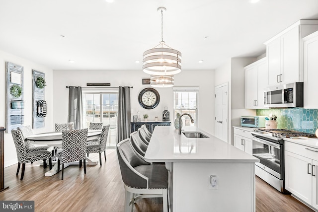 kitchen with wood finished floors, a sink, light countertops, appliances with stainless steel finishes, and backsplash