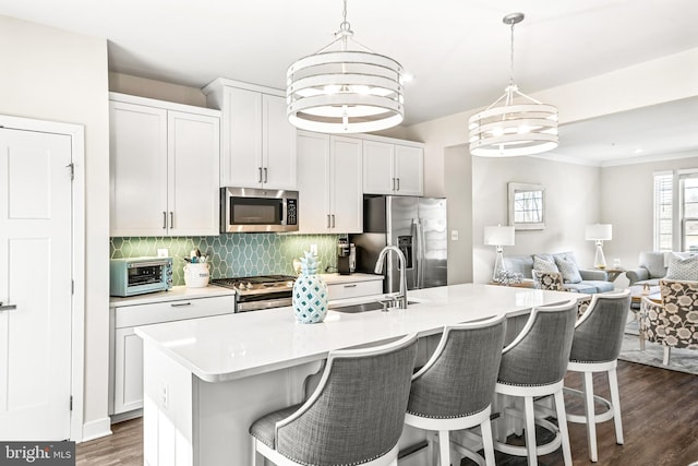 kitchen with an inviting chandelier, a sink, decorative backsplash, stainless steel appliances, and open floor plan