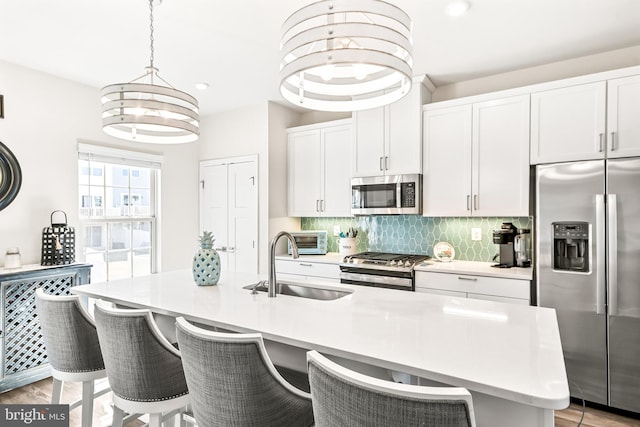 kitchen with light wood finished floors, a sink, decorative backsplash, light countertops, and appliances with stainless steel finishes