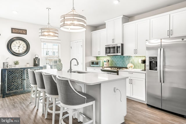 kitchen with an island with sink, a sink, backsplash, stainless steel appliances, and light wood-style floors