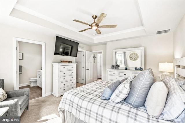 bedroom featuring visible vents, baseboards, light colored carpet, a tray ceiling, and ensuite bathroom