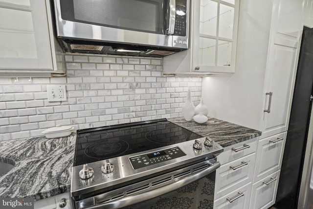 kitchen featuring stainless steel appliances, dark stone counters, tasteful backsplash, and white cabinetry