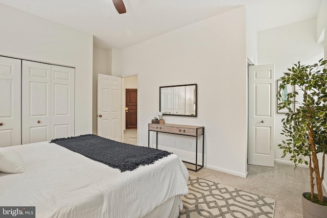 bedroom with a closet, light colored carpet, a ceiling fan, and baseboards