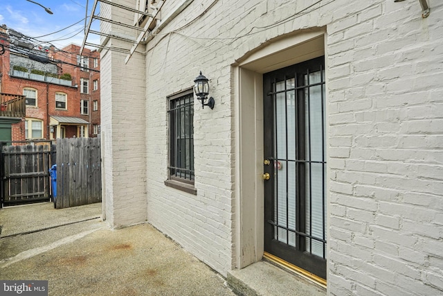 view of exterior entry with brick siding and fence