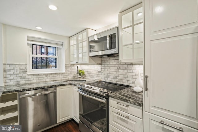 kitchen featuring tasteful backsplash, glass insert cabinets, white cabinets, stainless steel appliances, and a sink