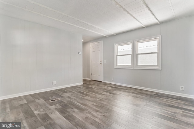 spare room featuring wood finished floors, visible vents, and baseboards