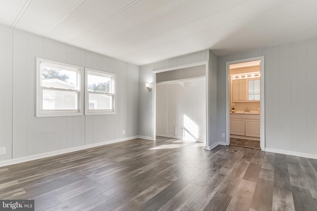 unfurnished bedroom with baseboards, dark wood-style flooring, a sink, a closet, and ensuite bathroom