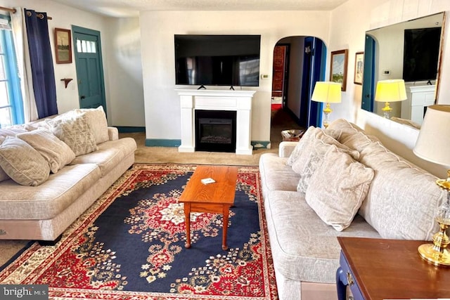 carpeted living area featuring arched walkways, a glass covered fireplace, and baseboards