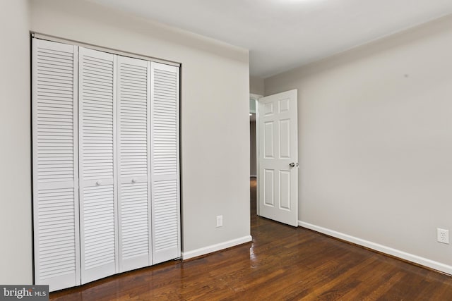 unfurnished bedroom with baseboards, a closet, and dark wood-style flooring