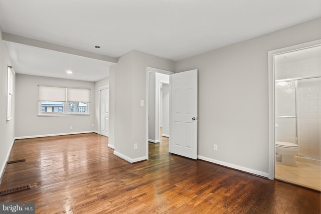 unfurnished bedroom featuring visible vents, baseboards, ensuite bath, and wood finished floors