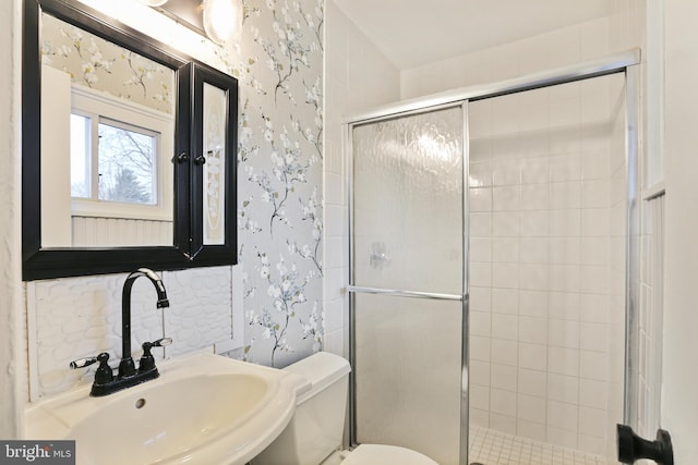 bathroom featuring wallpapered walls, a shower stall, toilet, and a sink