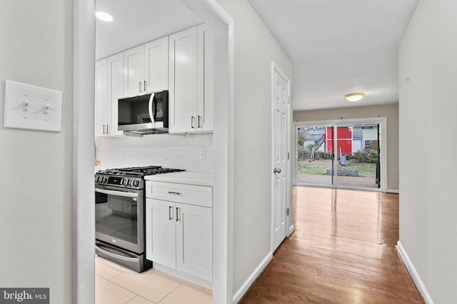 kitchen featuring decorative backsplash, white cabinets, stainless steel appliances, and baseboards