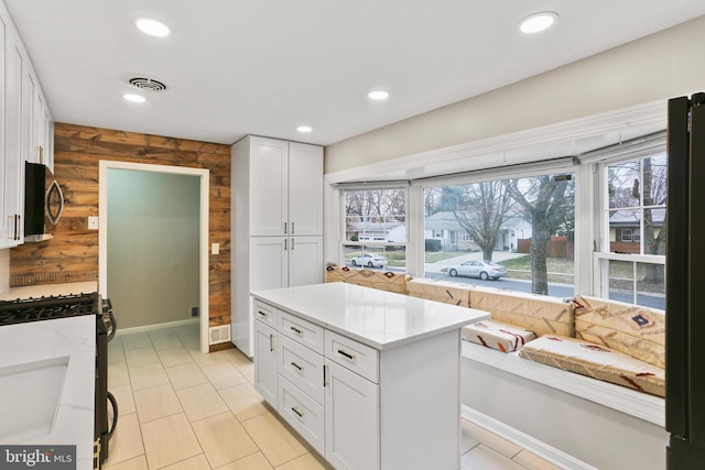 kitchen featuring wooden walls, gas stove, visible vents, white cabinets, and stainless steel microwave