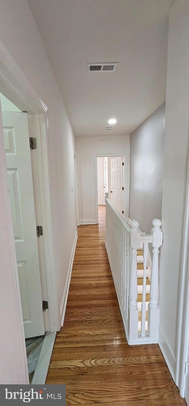 corridor with visible vents, an upstairs landing, baseboards, and wood finished floors