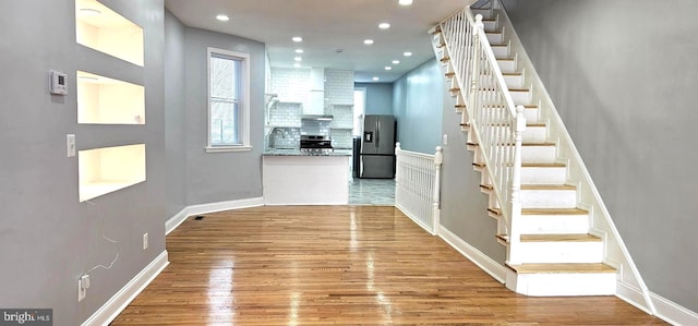 corridor featuring a sink, light wood-style floors, recessed lighting, and stairs