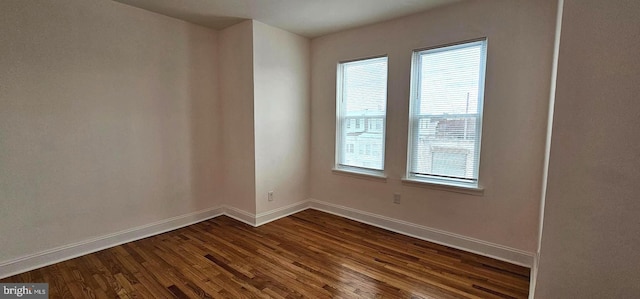 spare room featuring dark wood-type flooring and baseboards