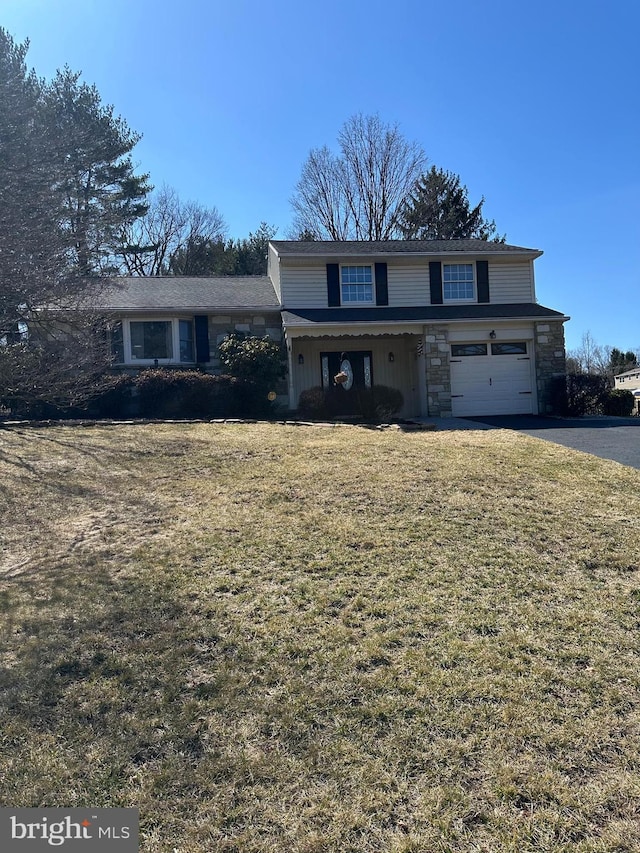 traditional-style house with driveway, stone siding, a front lawn, and an attached garage