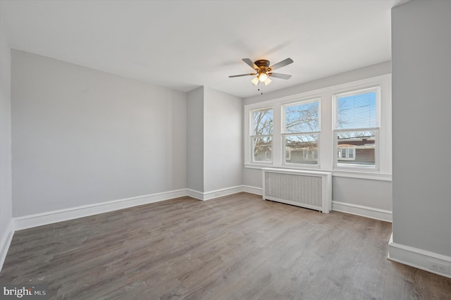 unfurnished room featuring baseboards, a ceiling fan, wood finished floors, and radiator heating unit