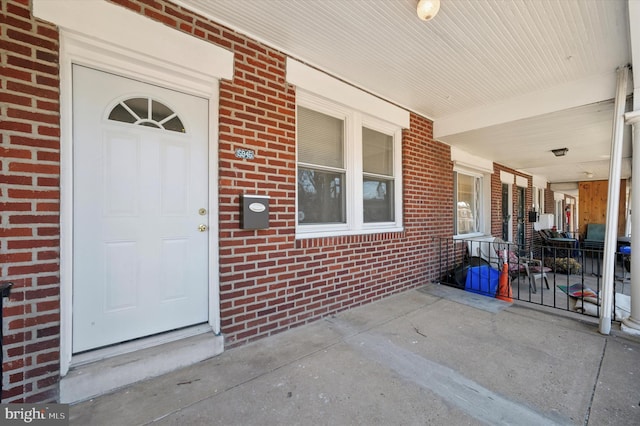 view of exterior entry with brick siding and covered porch