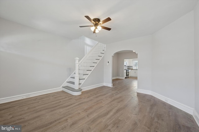 unfurnished living room featuring stairs, wood finished floors, arched walkways, and baseboards