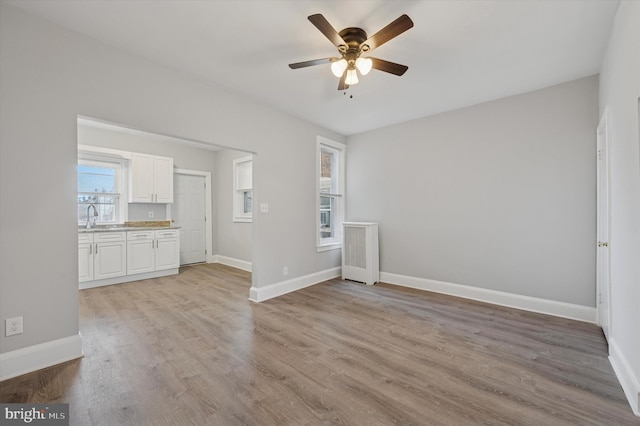 unfurnished room with a sink, baseboards, a ceiling fan, and light wood finished floors