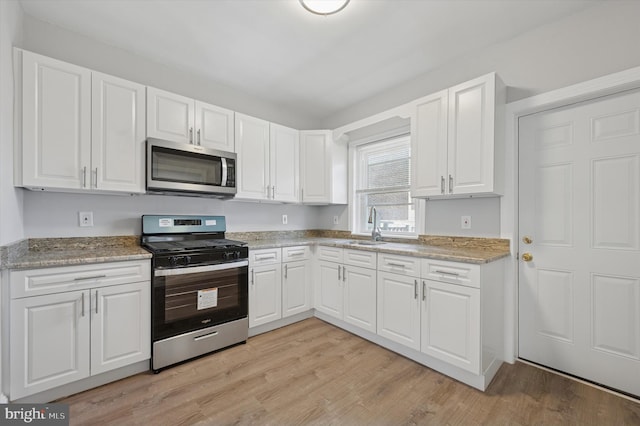 kitchen featuring white cabinets, light wood-type flooring, appliances with stainless steel finishes, and a sink