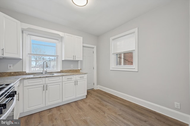 kitchen featuring a sink, stainless steel range oven, baseboards, and white cabinetry