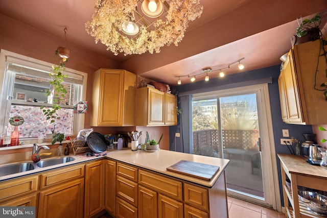 kitchen with a sink, a peninsula, light tile patterned floors, and light countertops