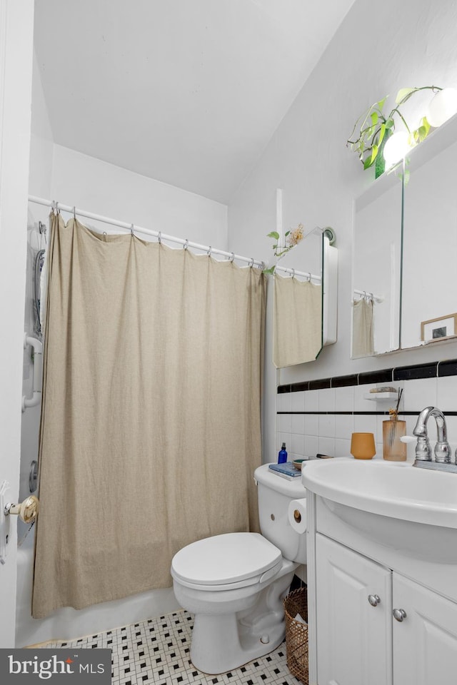 full bath with shower / bath combo with shower curtain, toilet, tile walls, wainscoting, and vanity