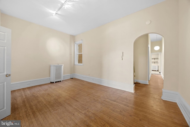 spare room with hardwood / wood-style floors, radiator heating unit, arched walkways, rail lighting, and baseboards