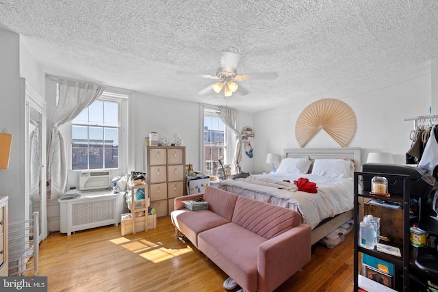 bedroom featuring a ceiling fan, wood finished floors, radiator heating unit, and a textured ceiling