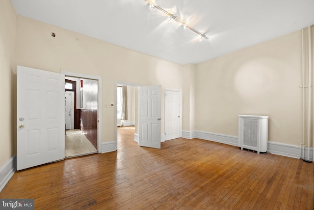 empty room with baseboards, hardwood / wood-style floors, and track lighting